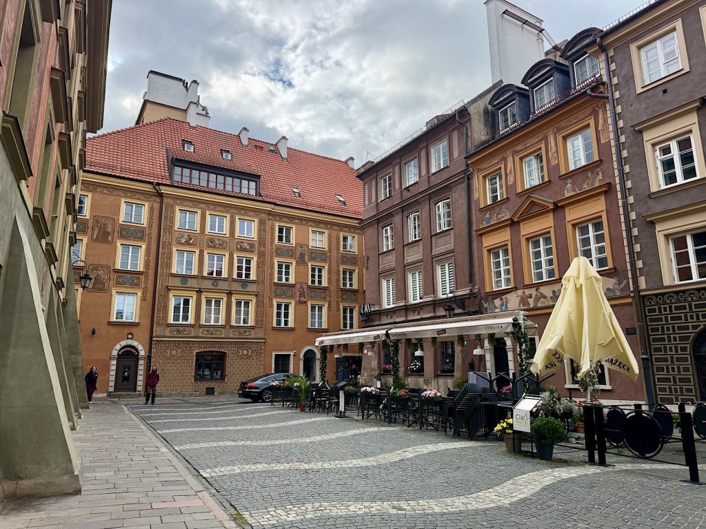 Charming cobblestone street in a historic district, featuring colorful buildings with detailed facades and outdoor seating at a café.