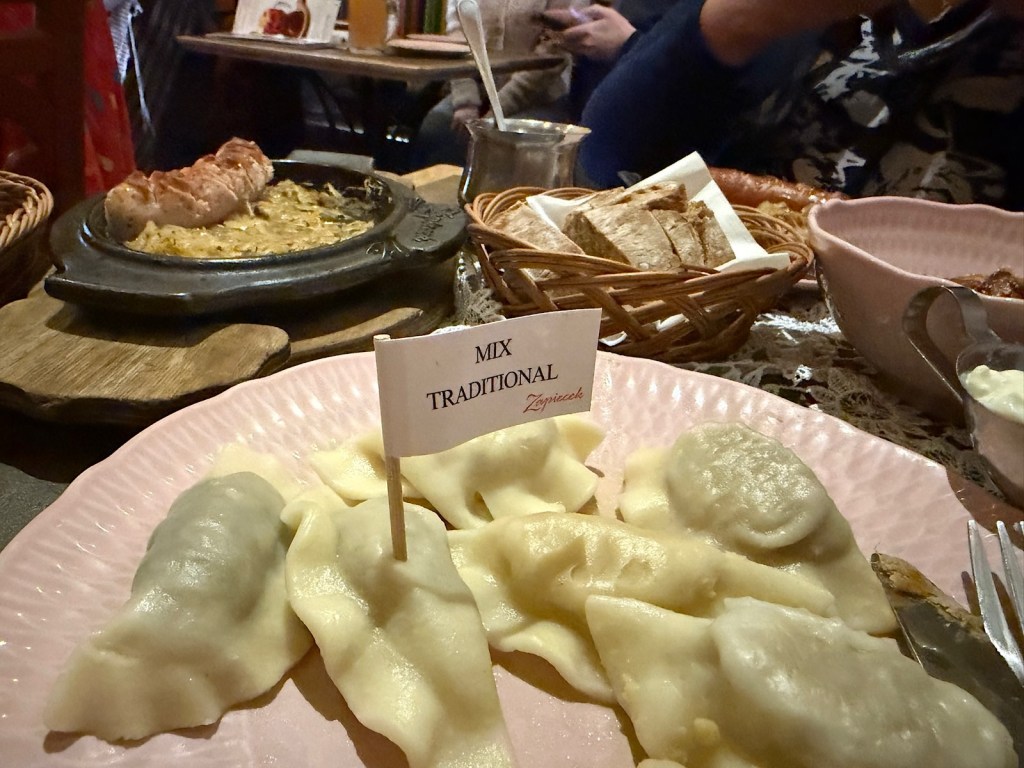 A plate of traditional mixed dumplings labeled 'MIX TRADITIONAL,' with a variety of fillings, alongside a serving of grilled meat and bread in a cozy dining setting.
