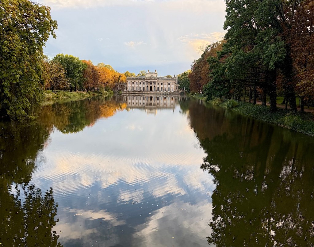 Reflections of a grand building in a calm lake surrounded by colorful autumn trees.