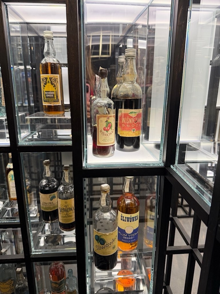 A display case featuring various bottles of spirits, including ginger liqueur and multiple fruit-flavored vodkas, elegantly arranged on glass shelves.