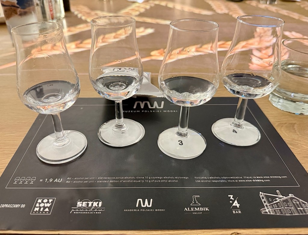 Four small glass tasting cups with vodka, placed on a black tasting menu at a bar.