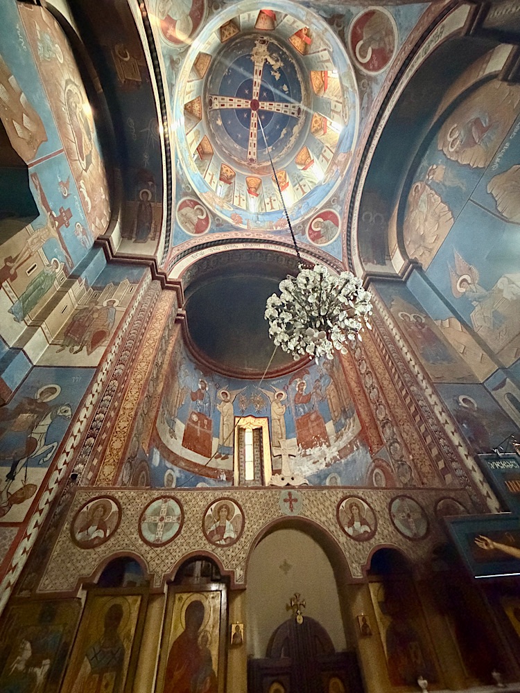Interior view of a beautifully painted church, showcasing ornate frescoes on the dome and walls, with a chandelier in the center.
