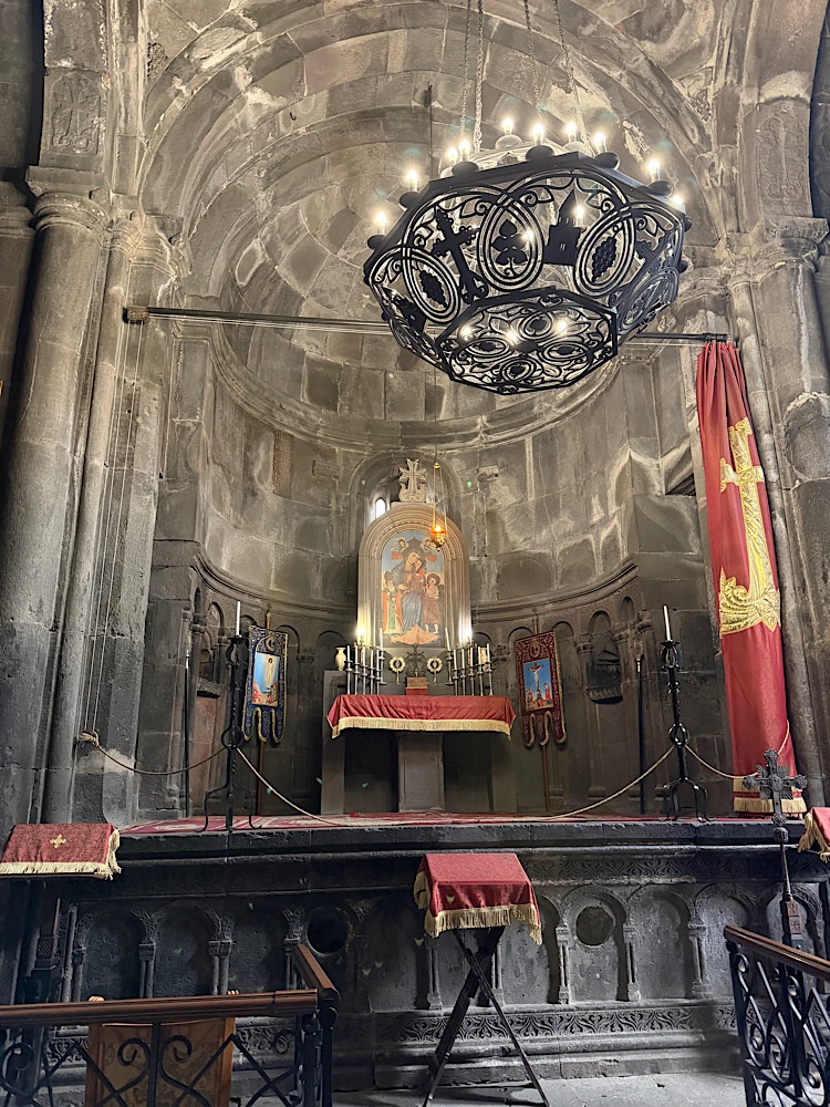 Interior view of a church featuring a beautifully adorned altar with candles, framed religious icons, and a decorative chandelier hanging from the vaulted ceiling.