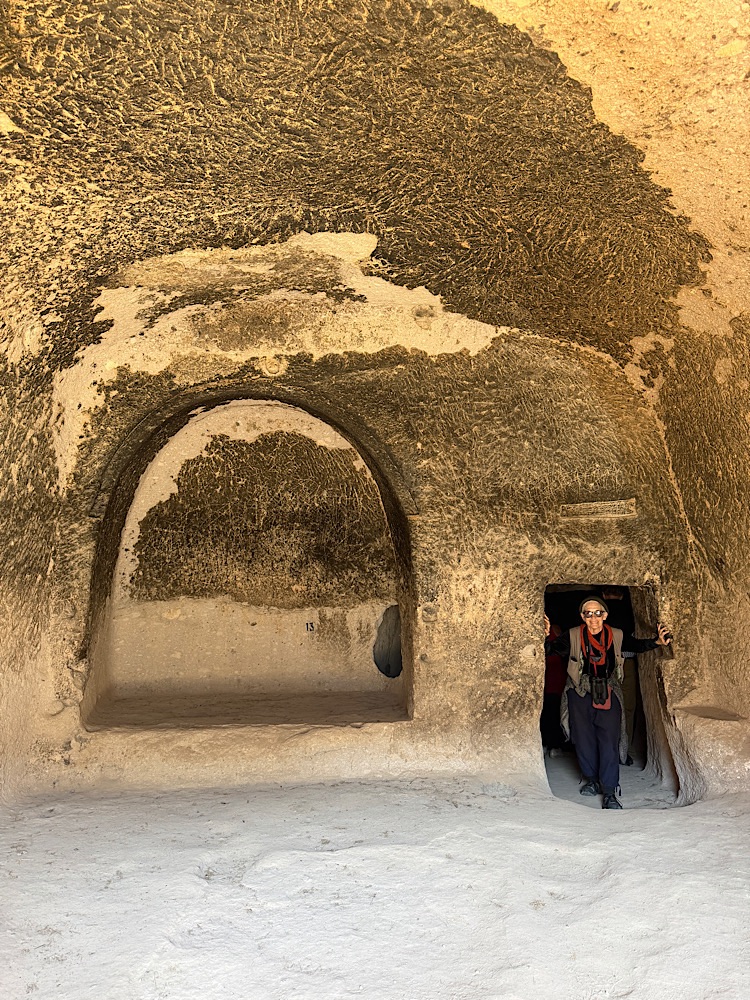 Interior of a cave with textured walls, featuring a person standing at the entrance and a recessed area on the left.