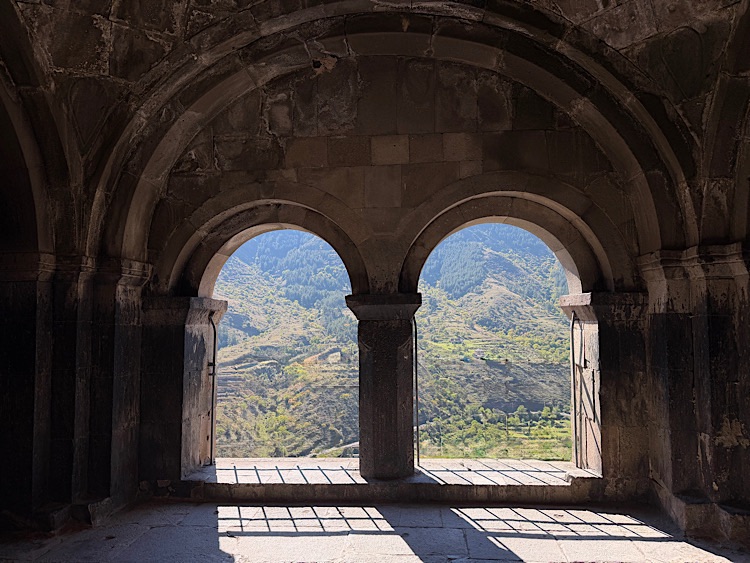Interior view of an ancient stone structure featuring arched windows that frame a mountainous landscape outside.